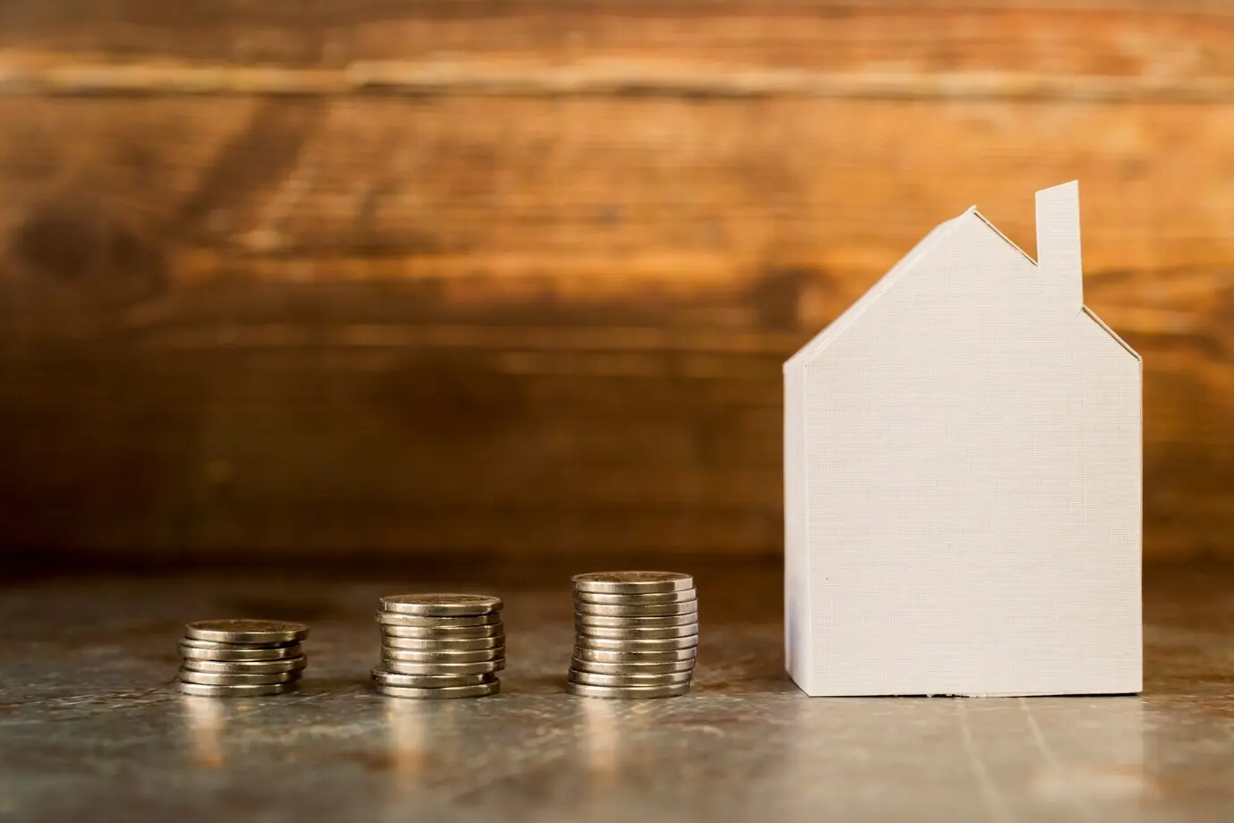 A growing stack of coins next to a paper house on the surface.