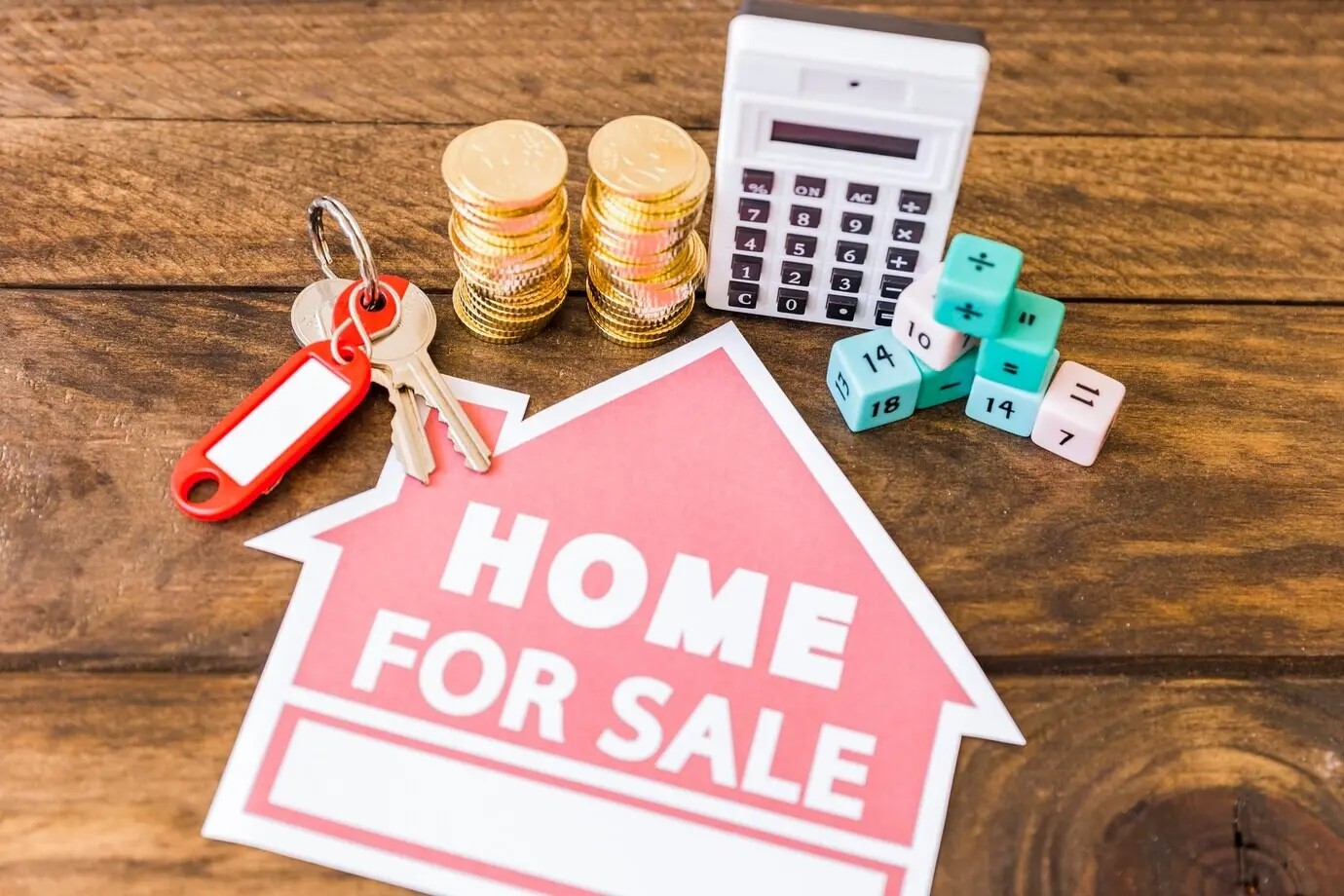 Overhead view of a calculator, math blocks, coin stacks, and a key with a home-for-sale icon.